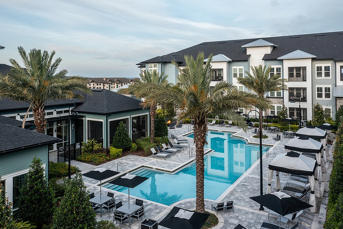 Aerial view of Cottonwood Clermont, a luxurious apartment complex featuring a pristine swimming pool surrounded by elegant palm trees and stylish lounge areas.