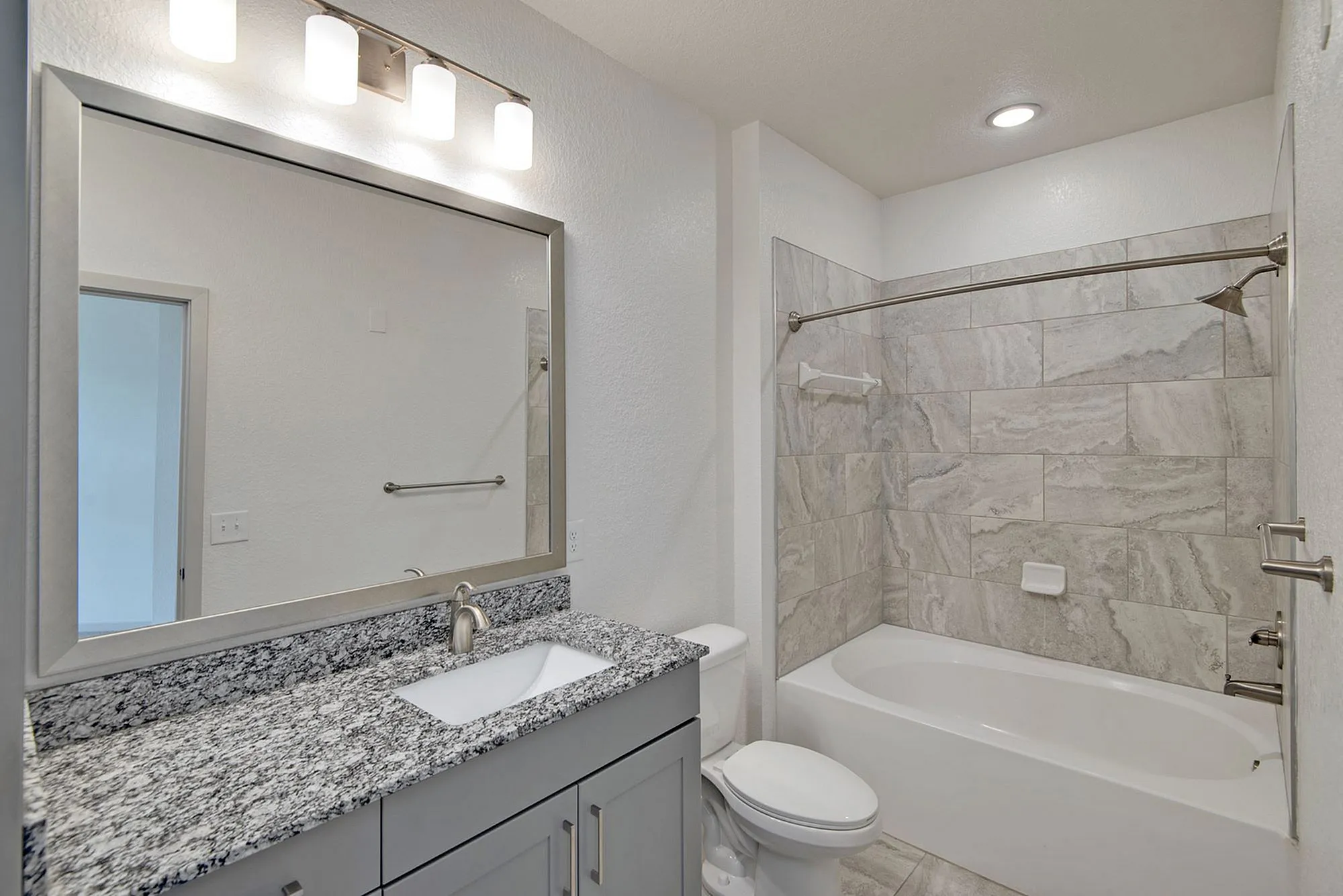 Modern bathroom at Cottonwood Clermont Apartments with sleek granite countertop, large mirror, and elegant tiled shower, offering a luxurious and contemporary feel.