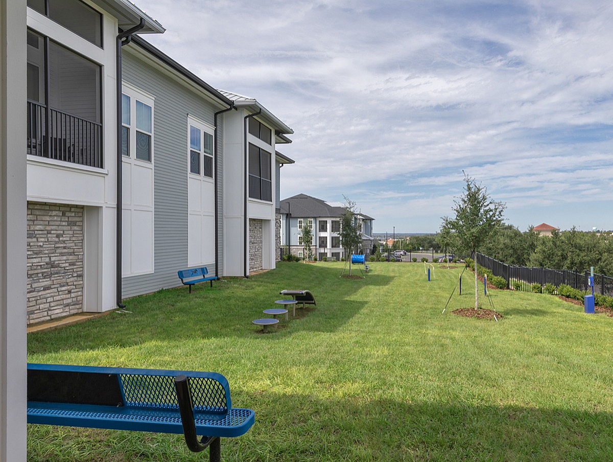 Exterior of Cottonwood Clermont showing the dog park with expansive green lawn, cozy benches, and modern architecture under a bright sky.