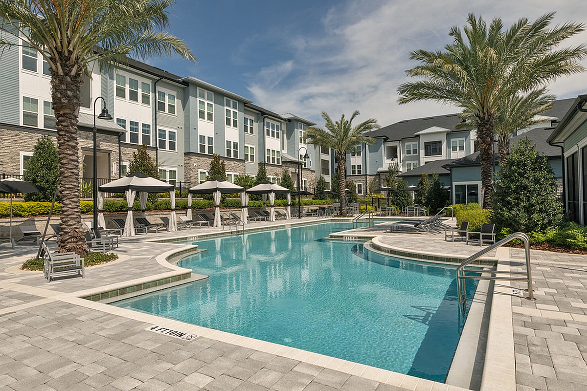 Luxurious apartment complex with a sparkling pool, surrounded by palm trees and elegant lounge seating, offering a resort-style living experience.