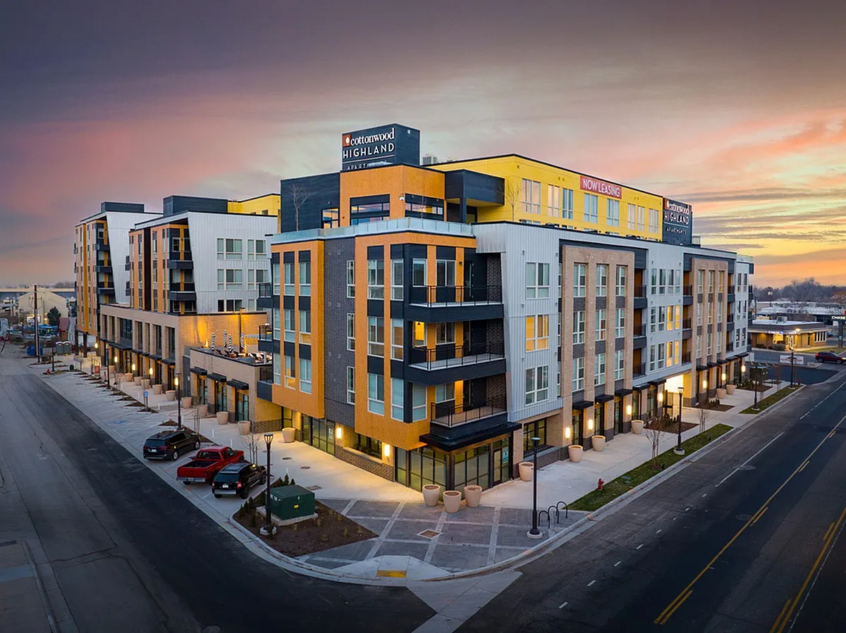 Exterior view of Cottonwood Highland, a modern urban apartment complex with vibrant colors and spacious balconies at sunset, showcasing contemporary design in a prime city location.
