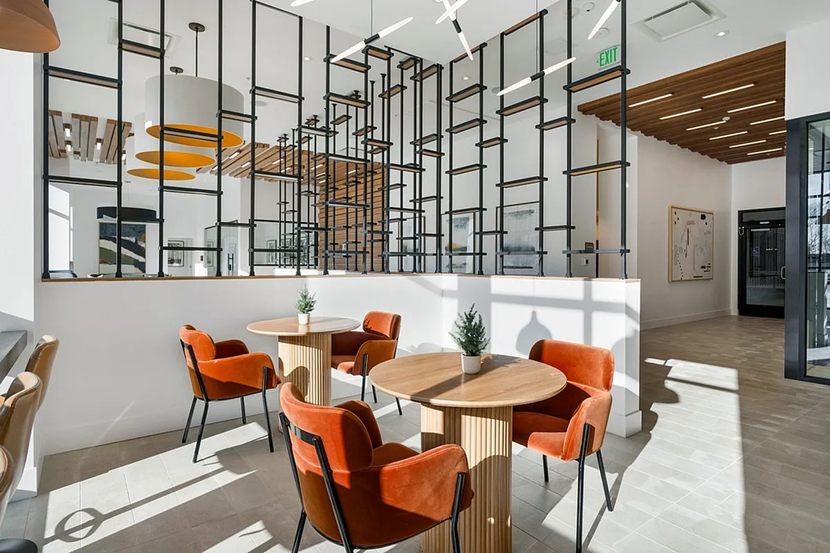 Modern and inviting coworking space at Cottonwood Highland Apartments with stylish seating, vibrant orange chairs, and warm natural light filtering through architectural elements.