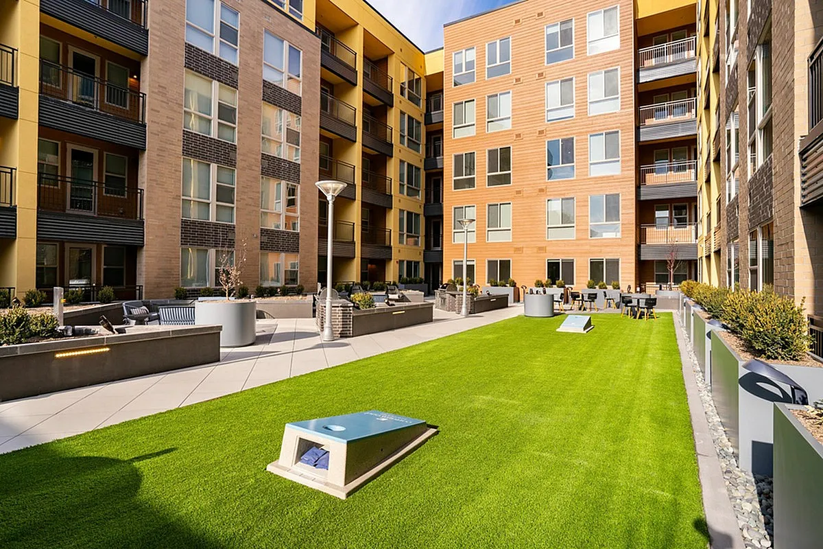 Inviting apartment courtyard at Cottonwood Highland featuring modern outdoor seating, lush green turf, and vibrant al fresco dining area.
