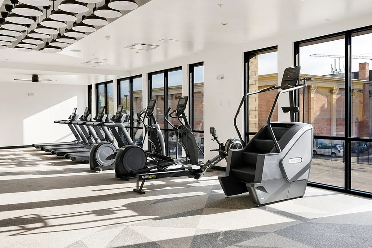 Bright, modern gym at Cottonwood Highland Apartments with state-of-the-art treadmills and cardio equipment, accented by panoramic windows and sleek lighting fixtures.