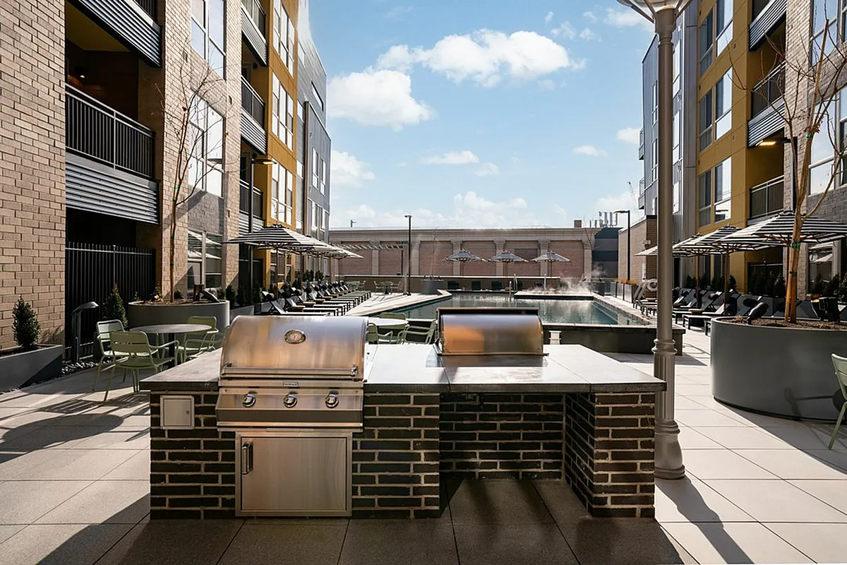 Cottonwood Highland Apartments' courtyard featuring a sleek outdoor grill area and inviting poolside seating with sunlit ambiance.