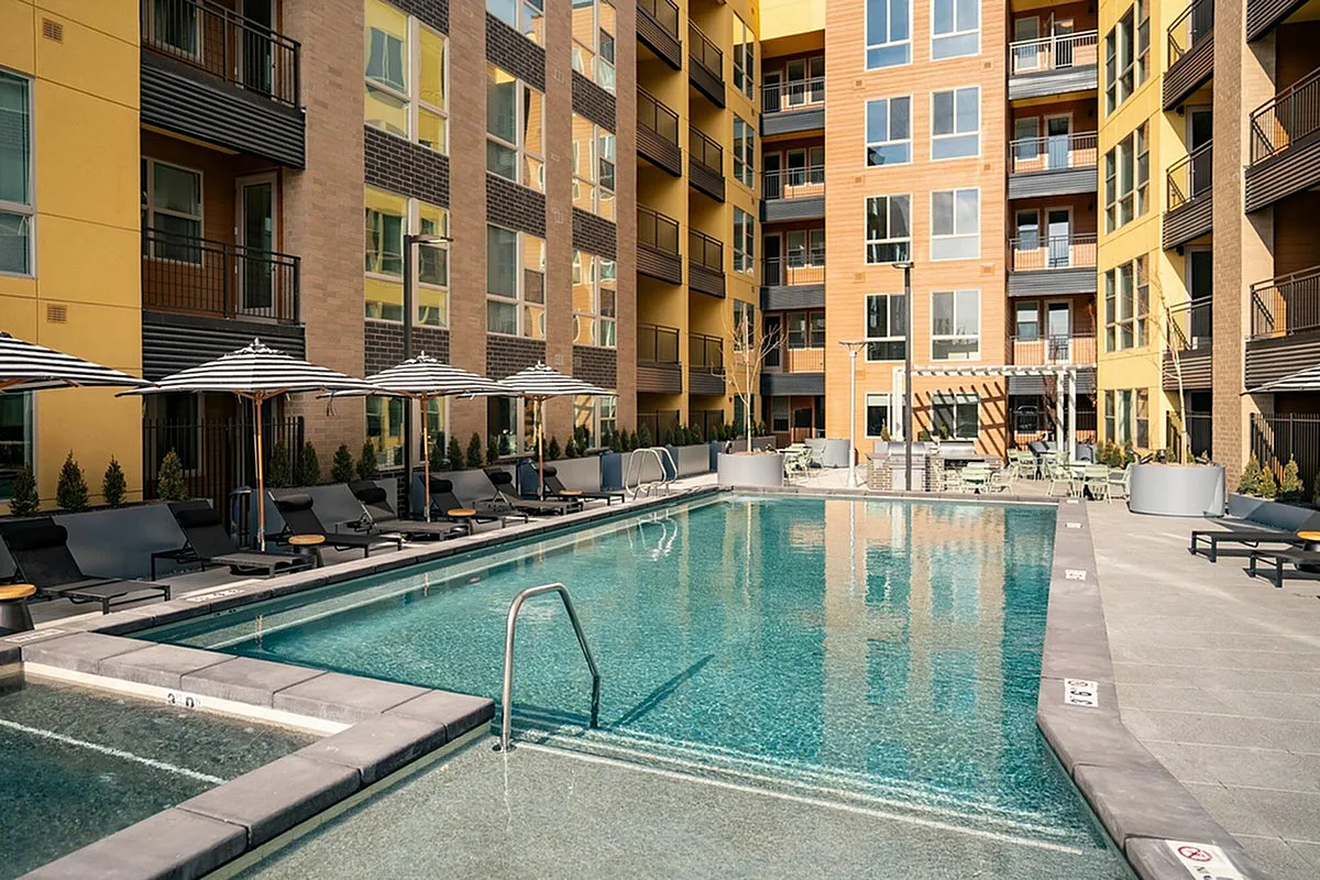 View of Cottonwood Highland Apartments with a sparkling outdoor pool, modern lounge chairs, and stylish umbrellas, perfect for relaxation and entertainment.