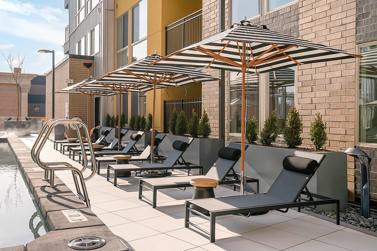 Chic outdoor pool area at Cottonwood Highland Apartments with modern loungers and stylish striped umbrellas, perfect for relaxation under the sun.