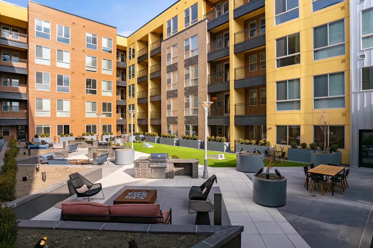 View of Cottonwood Highland Apartments with a vibrant courtyard featuring seating areas, barbecue grills, and lush greenery.