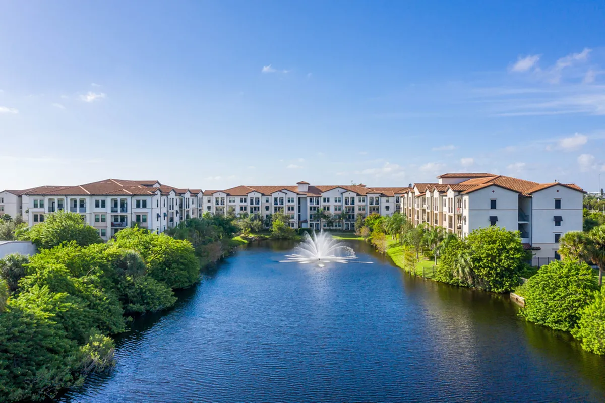 Elegant lakeside apartments with terracotta roofs, surrounded by lush greenery and featuring a serene fountain view at Cottonwood Lighthouse Point..