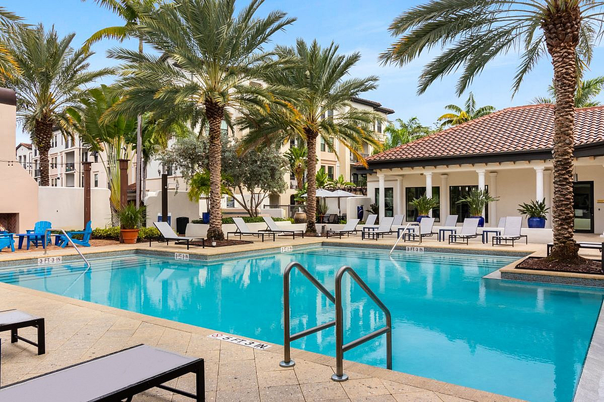 View of Cottonwood Lighthouse Point Apartment featuring a pristine swimming pool surrounded by elegant loungers and lush palm trees, offering a tropical resort-like atmosphere.