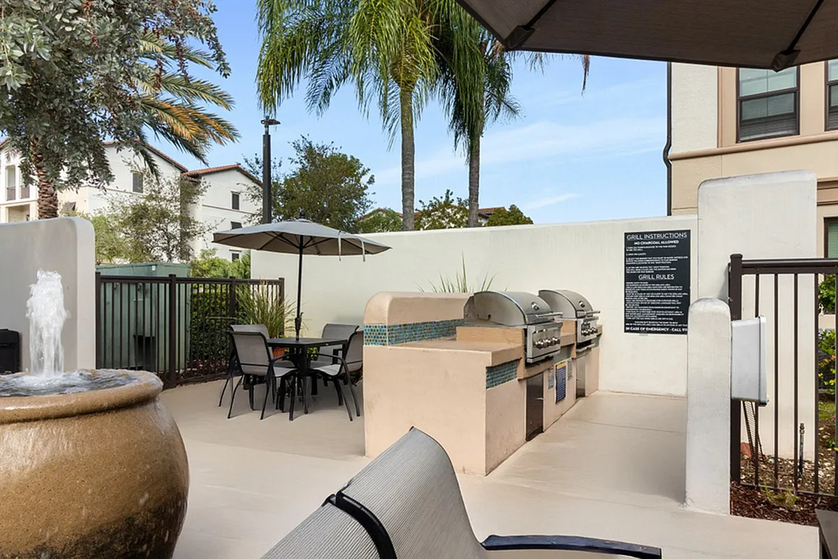 Charming outdoor patio at Lighthouse Point Apartments with modern grills, cozy seating, and lush palm trees, ideal for social gatherings.