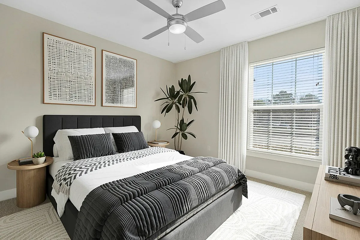 Modern bedroom at Cottonwood Reserve Apartments with sleek black and white decor, elegant ceiling fan, and ample natural light from a large window.