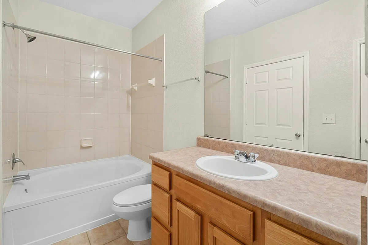 Bright, modern bathroom at Cottonwood Reserve Apartments featuring a sleek tub with beige tile surround, and a stylish vanity with ample storage.