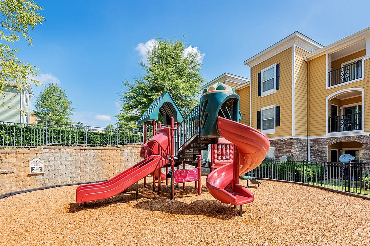 Charming playground at Cottonwood Reserve Apartments with vibrant red slides surrounded by lush greenery and stylish buildings.