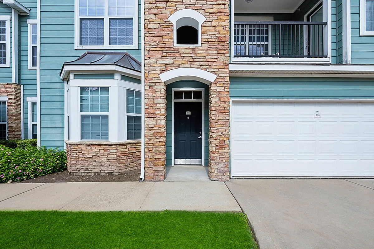 Elegant apartment facade at Cottonwood Ridgeview Apartments featuring stone accents, large windows, and a welcoming pathway with lush green lawn.