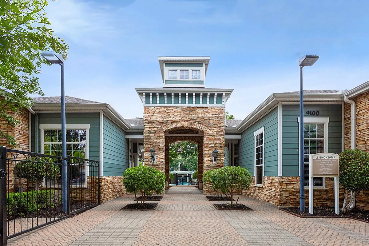 Inviting apartment leasing center at Cottonwood Ridgeview Apartments with modern architecture, stone accents, and lush greenery leading to a welcoming entrance.