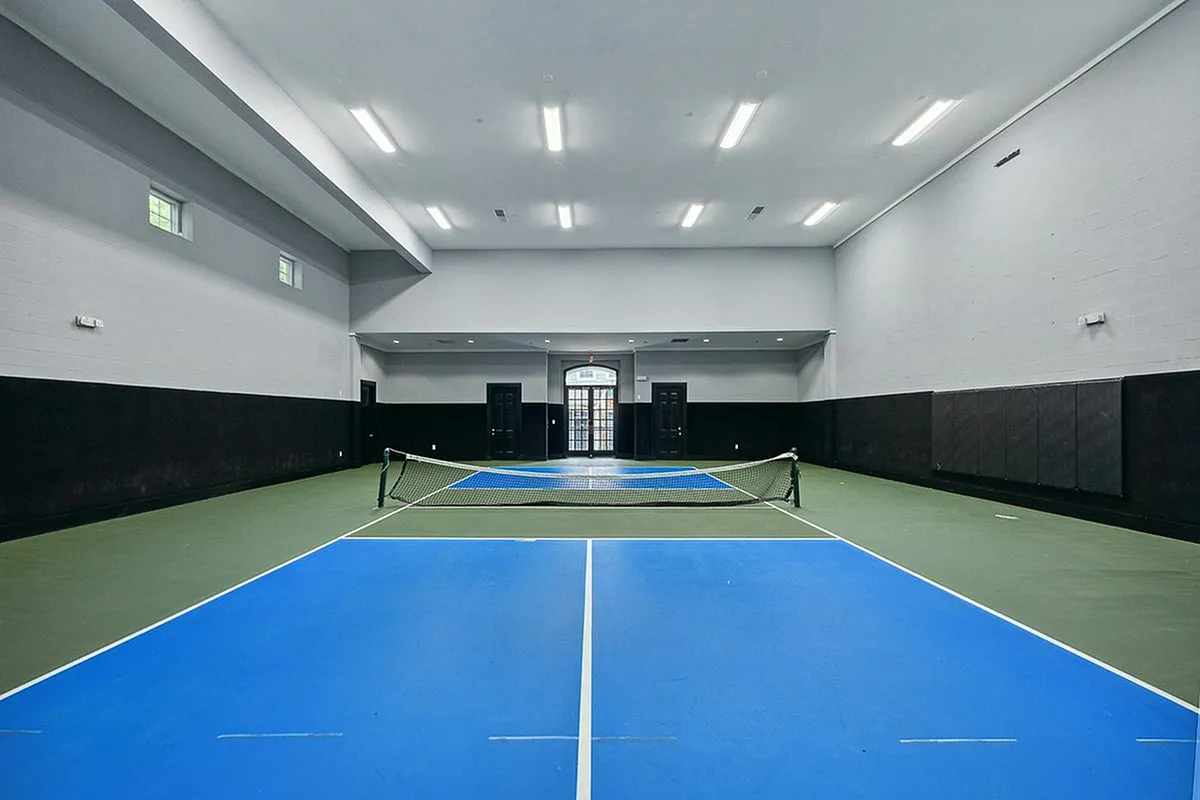 Spacious indoor pickleball court at Cottonwood Ridgeview Apartments with vibrant blue flooring, perfect for year-round exercise and entertainment.