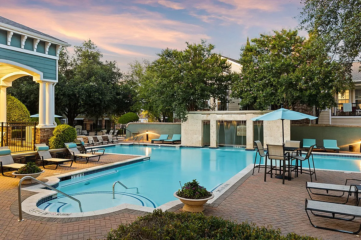 Luxurious apartment complex pool area featuring elegant loungers, umbrellas, and lush greenery under a vibrant sunset skyat Cottonwood Ridgeview Apartments.