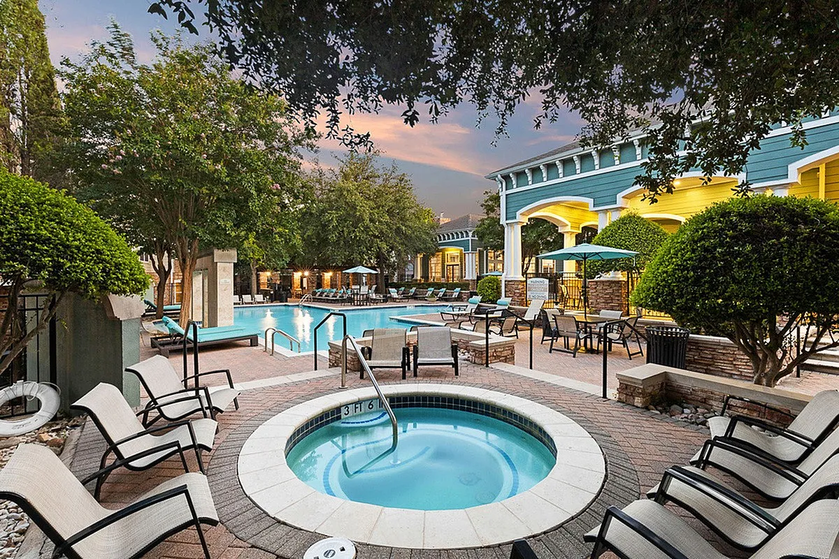Elegant evening view at Cottonwood Ridgeview Apartments of a luxurious pool area with a sparkling spa, surrounded by stylish lounge chairs and lush greenery, perfect for relaxation and entertaining.