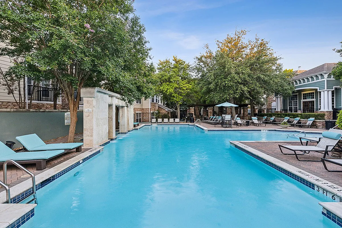 Inviting outdoor pool area at Cottonwood Ridgeview Apartments with luxurious lounge chairs, surrounded by lush greenery and stylish architecture.