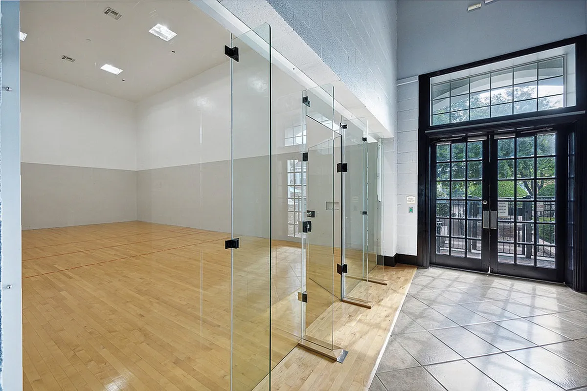 Modern indoor racquetball court at Cottonwood Ridgeview Apartments with sleek glass walls and polished wooden flooring, offering a bright and inviting space for recreational sports.