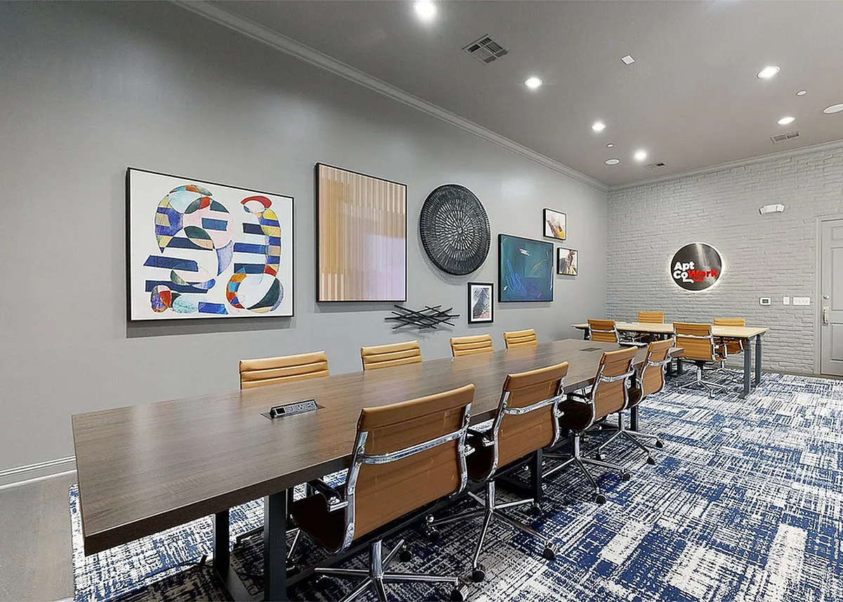 Modern conference room at Cottonwood Ridgeview Apartments with a long wooden table, sleek leather chairs, and vibrant artwork on the walls.