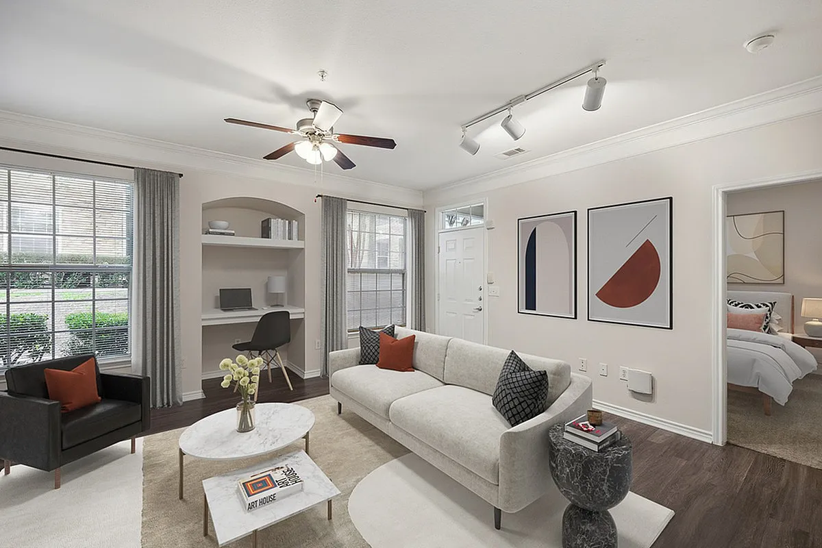 Inviting living room at Cottonwood Ridgeview Apartments with modern decor, featuring a cozy sofa, stylish armchair, and built-in workspace. Large windows offer abundant natural light, complemented by tasteful wall art.
