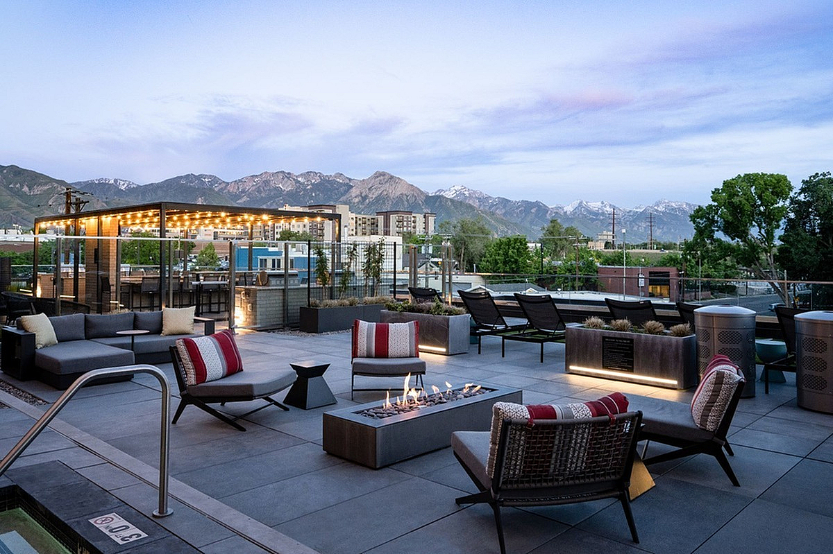 Elegant rooftop terrace at Sugarmont Apartments in SLC with cozy seating, fire pit, and stunning mountain views at sunset.
