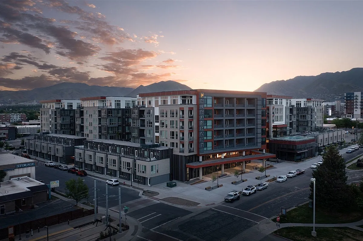 View of Sugarmont Apartmetns, a modern urban apartment complex at sunset with stunning Wasatch mountain backdrop, showcasing a vibrant community living experience in Sugar House.