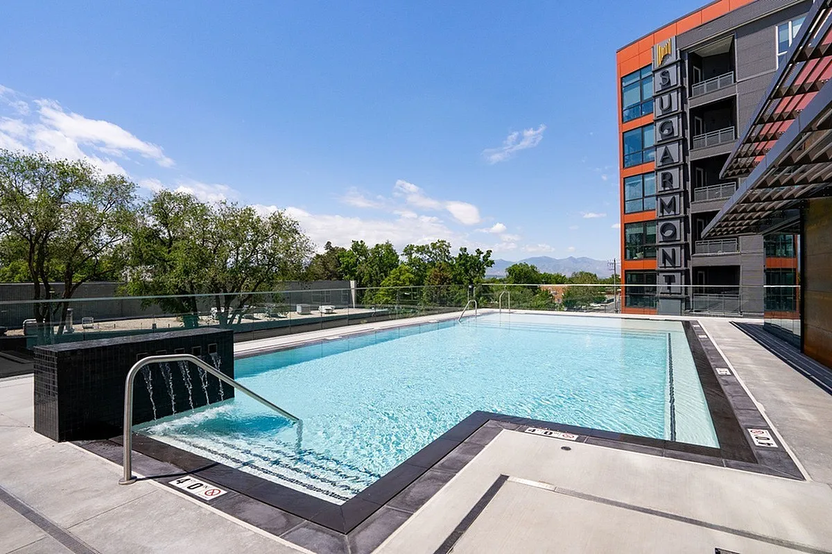Elegant rooftop swimming pool at Sugarmont Apartments with scenic mountain views and modern building architecture in Sugar House, Utah.