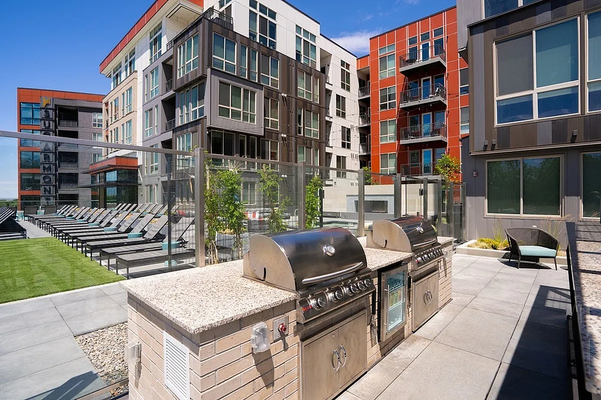 Modern apartment complex, Sugarmont Apartments, with vibrant architecture featuring spacious outdoor patio with stainless steel grills and comfortable seating area.