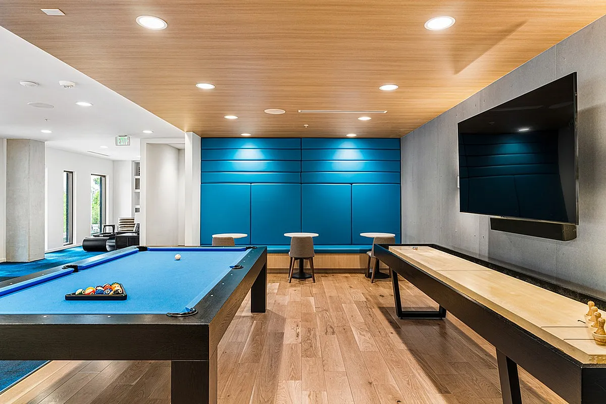 Modern entertainment room at Sugarmont Apartments featuring a sleek billiards table, shuffleboard, and large screen TV, ideal for leisure and relaxation.