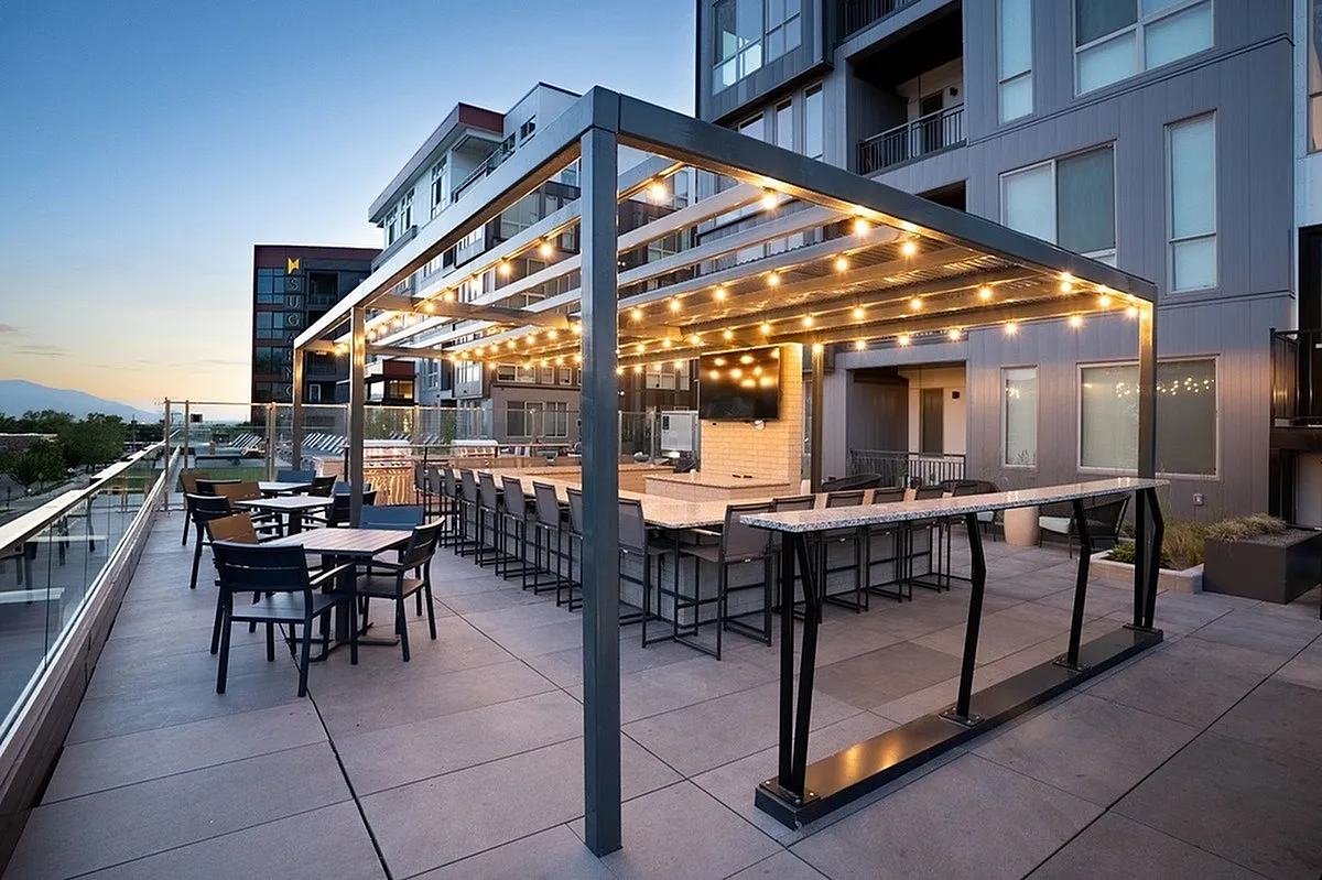 Elegant rooftop patio at Sugarmont in Salt Lake City, UT with modern pergola, sparkling string lights, and ample seating, offering stunning sunset views for social gatherings.