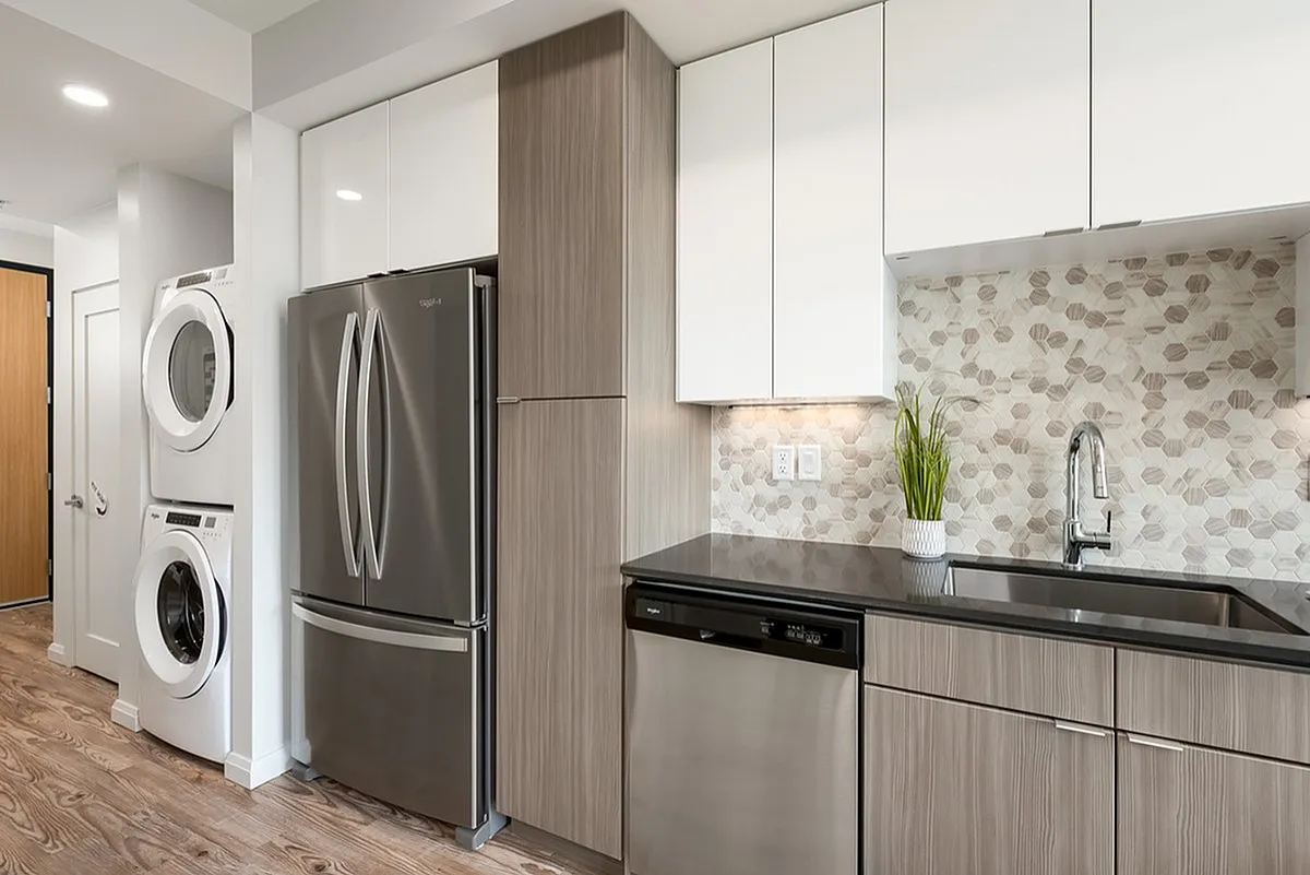 Modern kitchen at Sugarmont Apartments with stylish stainless steel appliances, elegant wood cabinetry, and a chic geometric backsplash.