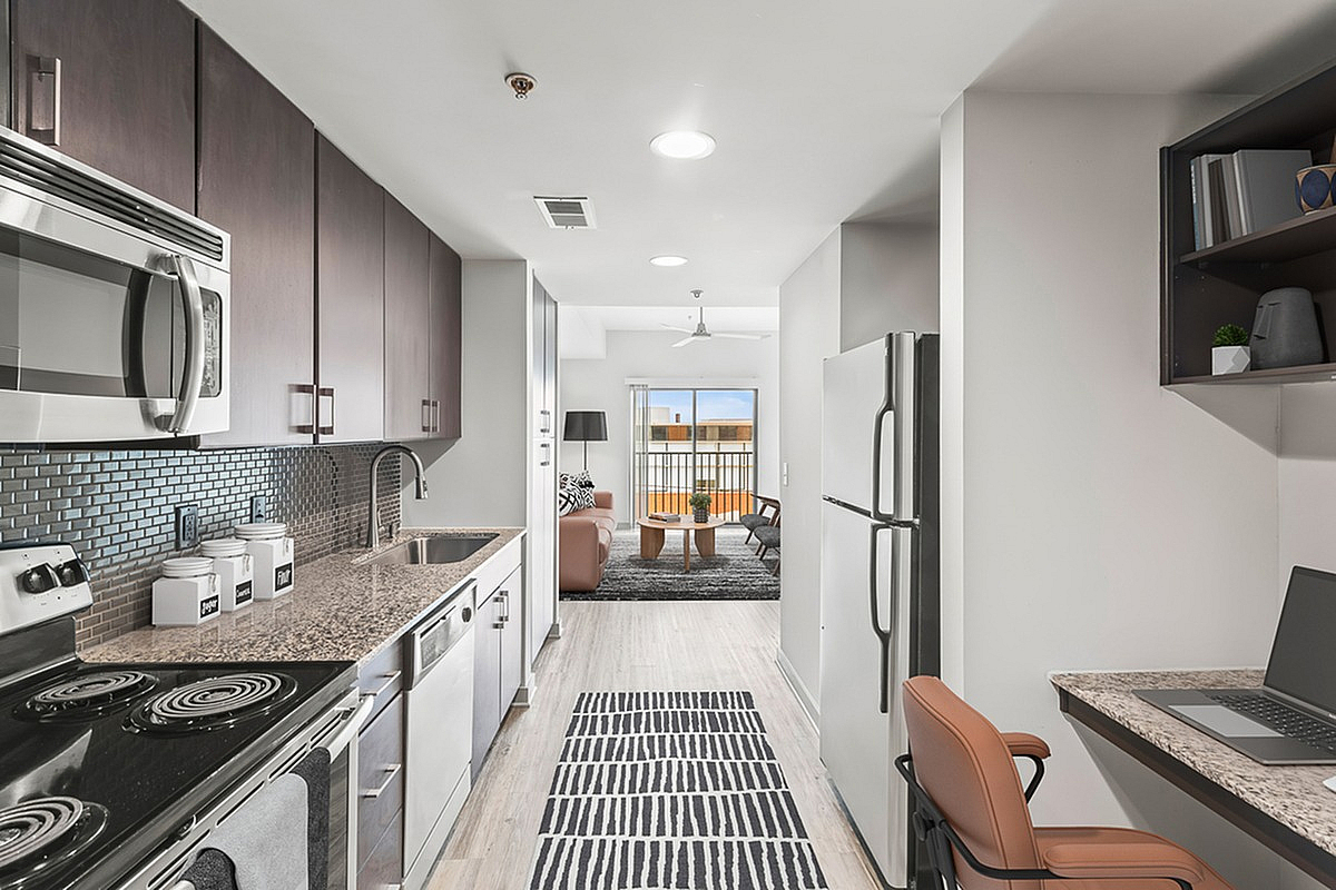 Modern apartment at Cottonwood Westside with sleek galley kitchen, stainless steel appliances, granite countertops, and an open living area with vibrant natural light.