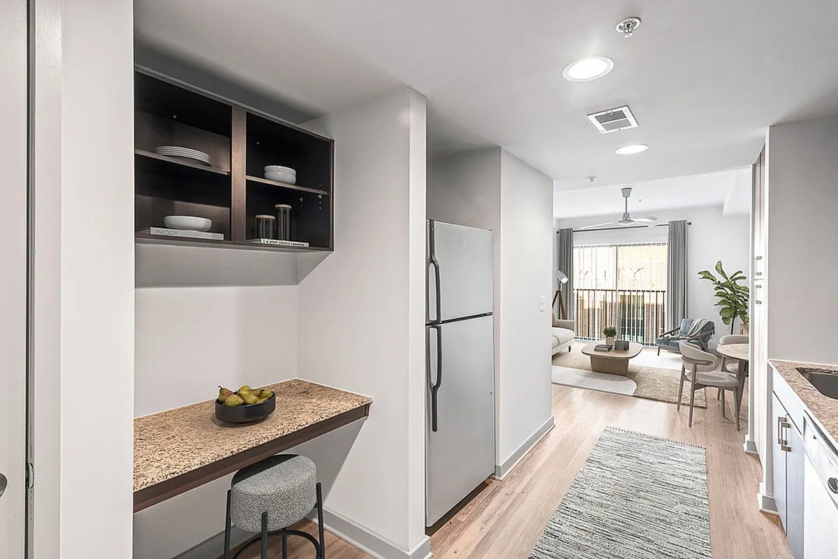 Inviting apartment kitchen at Cottonwood Westside with a cozy breakfast nook, stainless steel fridge, and a bright, airy living room view featuring stylish furnishings.