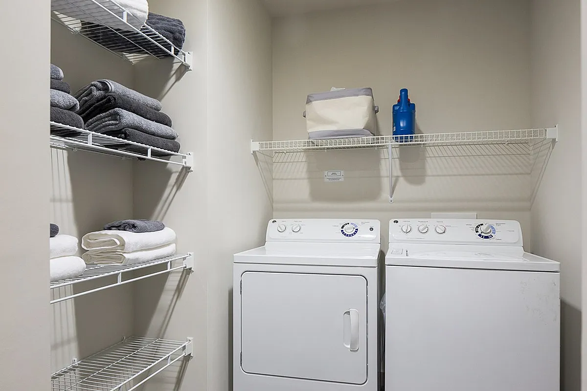 Modern laundry room at Cottonwood Westside with stacked towels and convenient shelving, featuring a washer and dryer in sleek white.