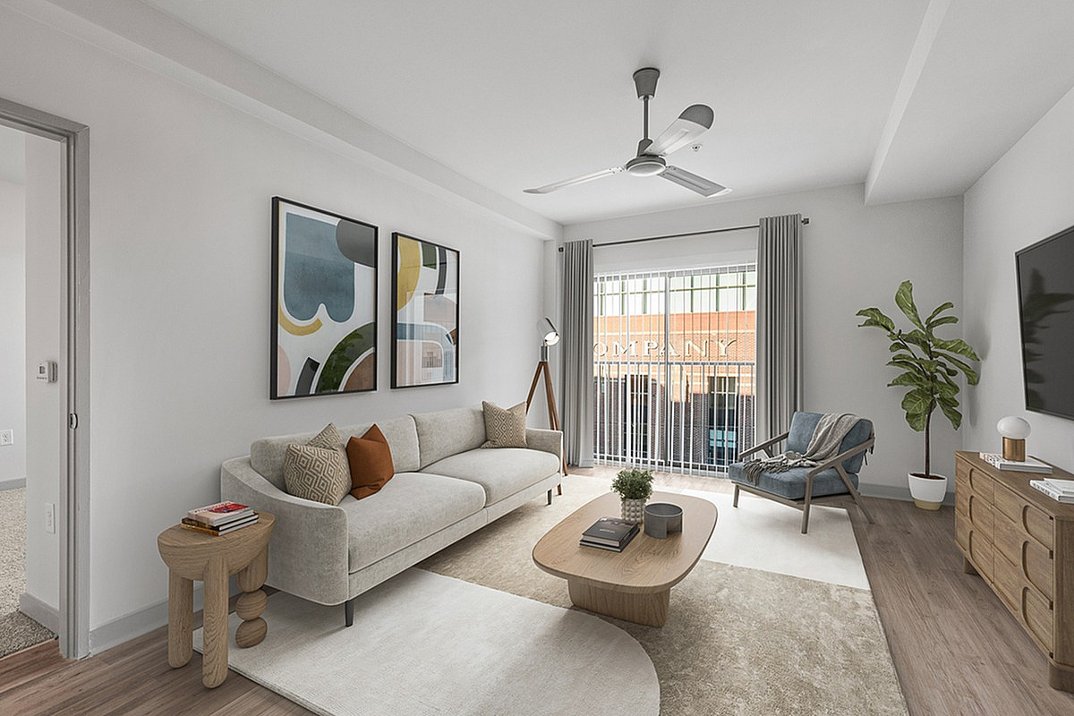 Modern living room with stylish beige sofa, colorful abstract art, and natural light streaming through large windows at Cottonwood Westside Apartments.