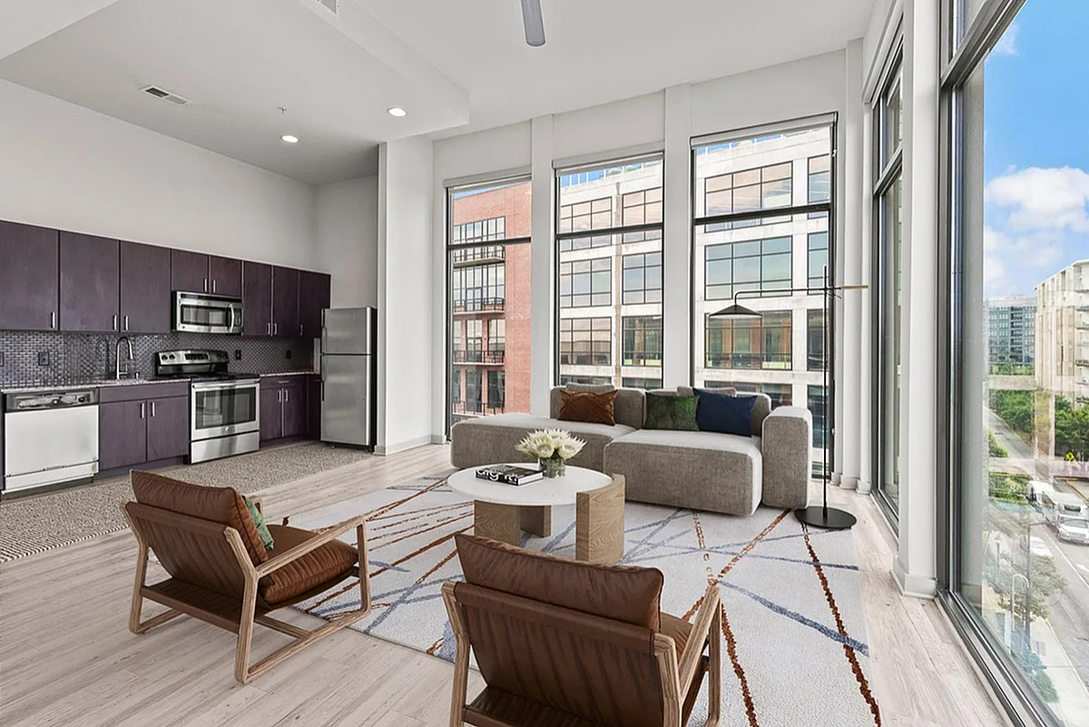 Contemporary open-plan apartment at Cottonwood Westside featuring a sleek kitchen with stainless steel appliances and a bright living area with floor-to-ceiling windows offering urban views.