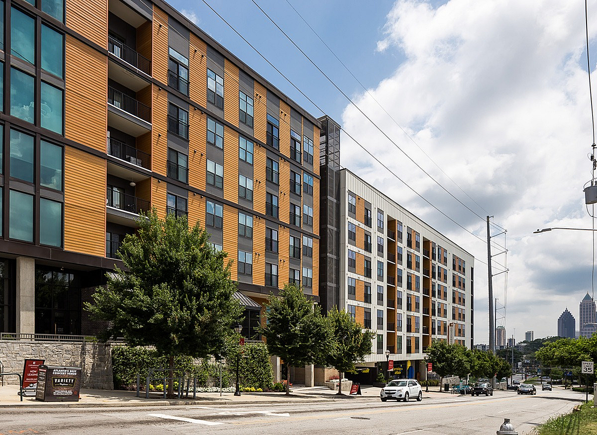 View of Cottonwood Westside, a contemporary apartment building exterior with striking orange accents, large windows, and lush greenery in an urban setting.