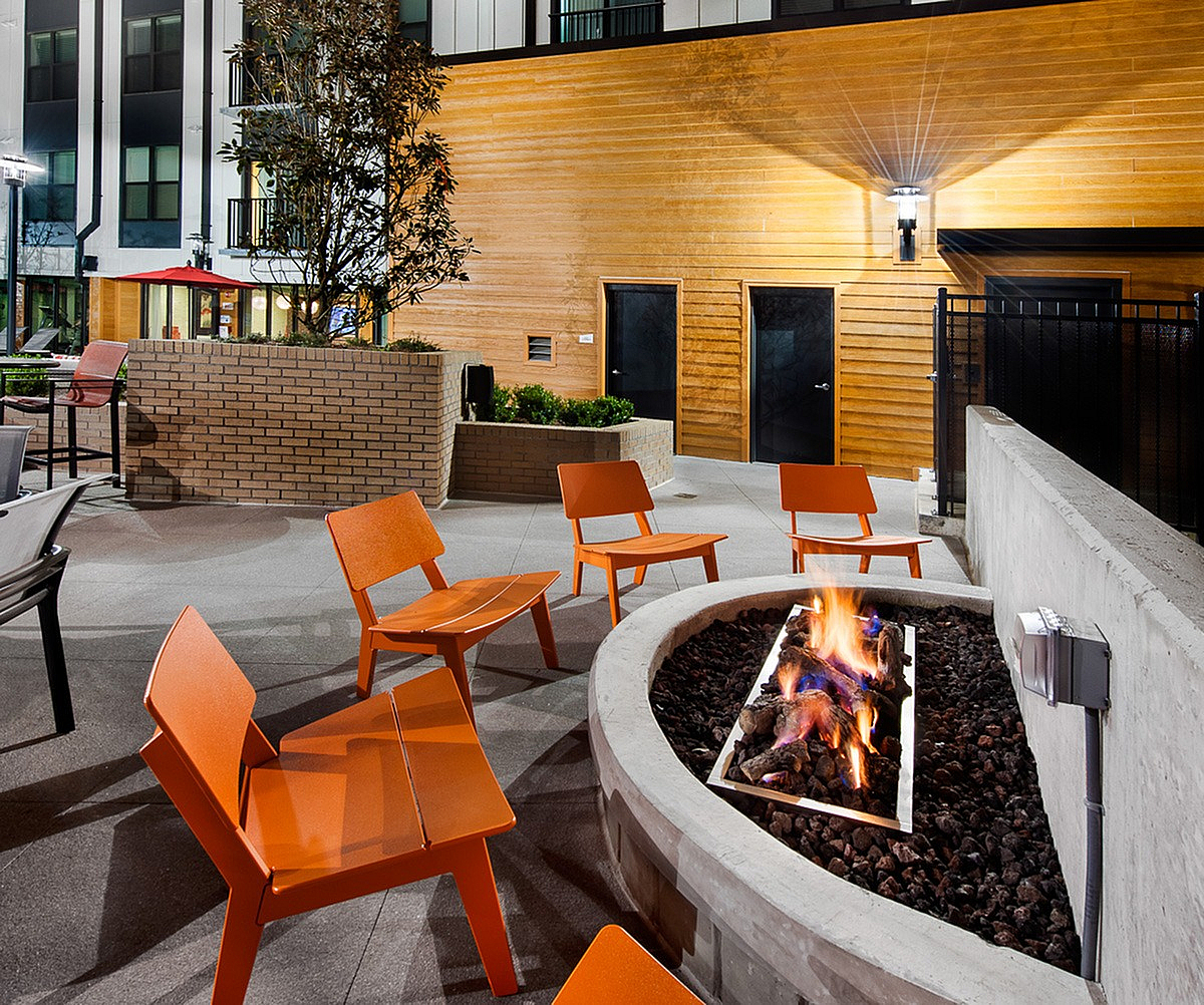 Inviting outdoor patio at Cottonwood Westside Apartments with modern orange chairs around a cozy fire pit, perfect for relaxed evening gatherings.