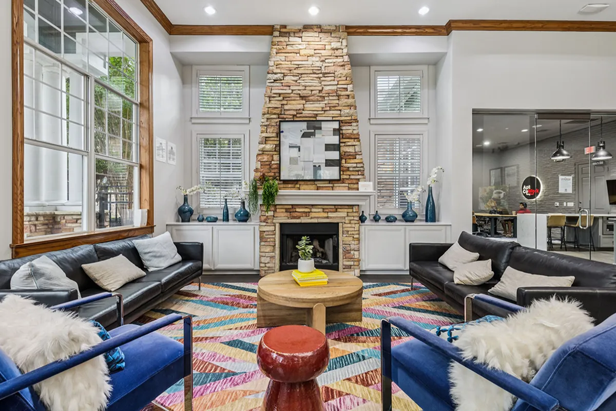Inviting study room with vibrant decor, featuring plush leather sofas, a colorful geometric rug, and a stone fireplace accent wall at Apt CoWork at Cottonwood Ridgeview in Plano TX
