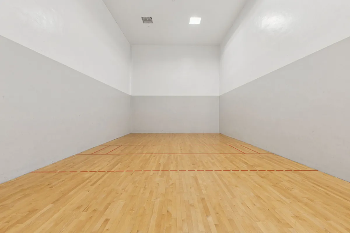Spacious indoor squash court with polished wooden floors and high white walls, offering a pristine playing environment at Cottonwood Ridgeview Apartments in Plano