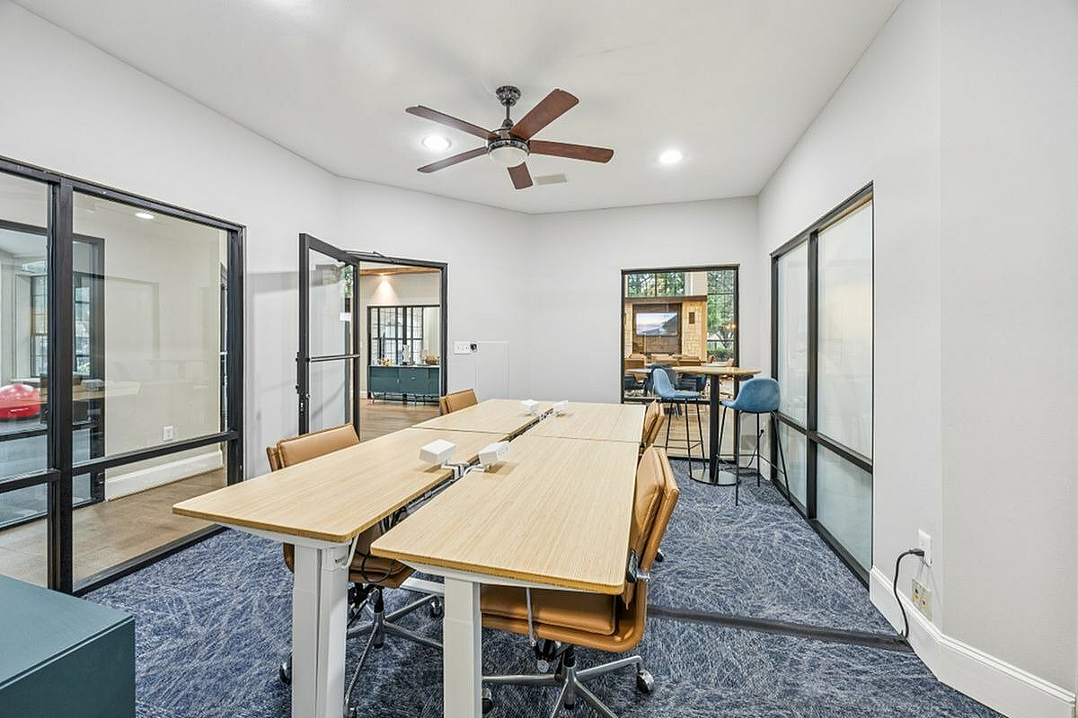 Modern conference room space with sleek glass partitions, adjustable desks, and stylish seating, perfect for dynamic work environments at Apt CoWork at Toscana at Valley Ridge Apartments in Lewisville Texas