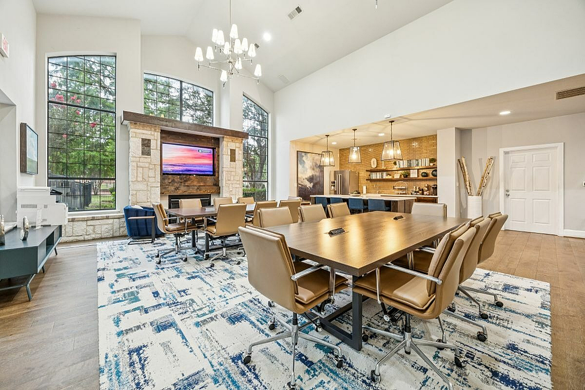 Elegant and spacious community lounge with modern design, featuring a large conference table, plush seating, and a stylish kitchen area under warm pendant lights at Apt CoWork at Toscana at Valley Ridge Apartments in Lewisville