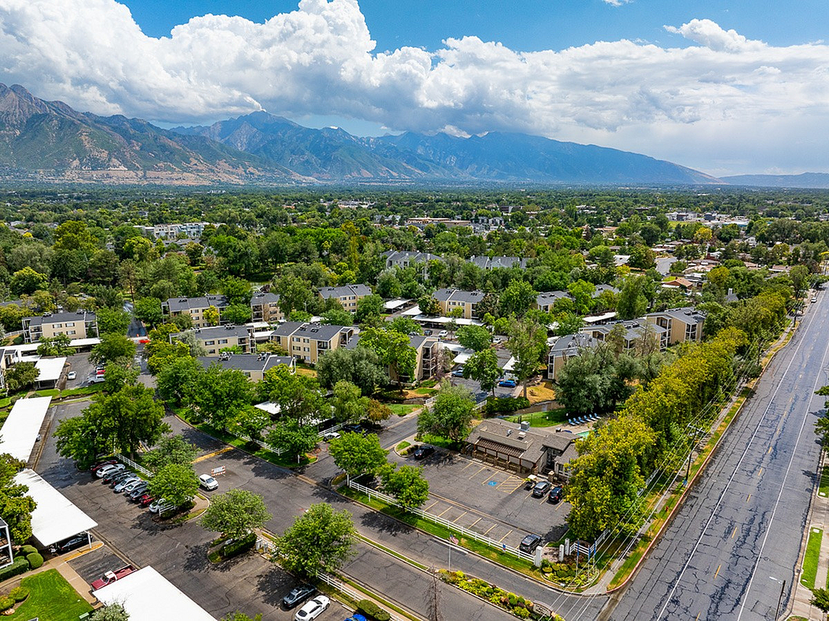 Scenic aerial view of a lush, vibrant SLC neighborhood surrounded by picturesque mountains and clear blue skies, perfect for relaxed living.