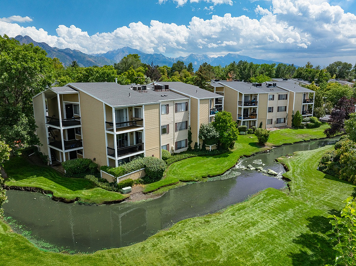 Beautiful apartment complex, Fox Point in Old Farm, with lush greenery and serene pond, nestled against stunning mountain backdrop in Salt Lake City.
