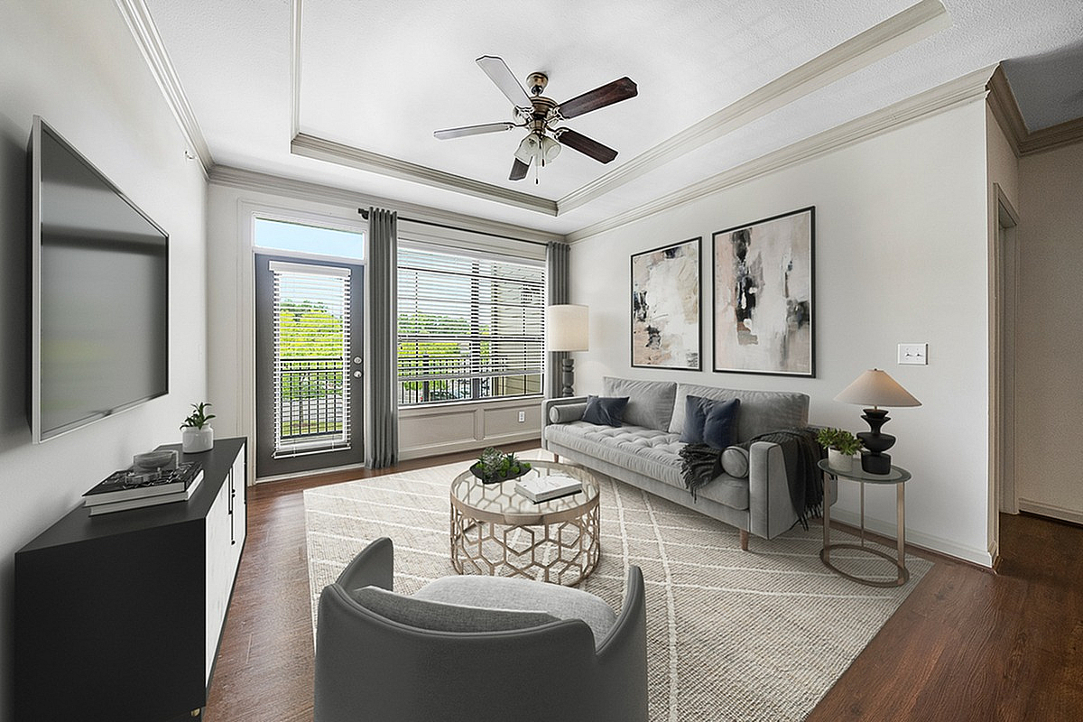 Elegant living room at Heights at Meridian Apartments with stylish decor, featuring a plush gray sofa, modern armchair, and large windows inviting natural light, complemented by framed artwork and a chic ceiling fan.