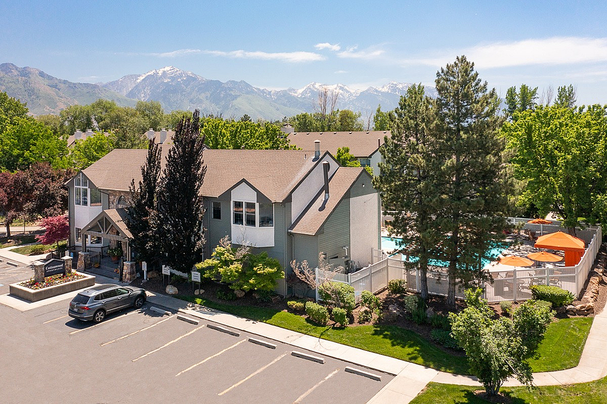 Charming apartment complex, Cottonwood Apartments, nestled in lush greenery with a stunning mountain backdrop, featuring a refreshing swimming pool and inviting outdoor spaces.