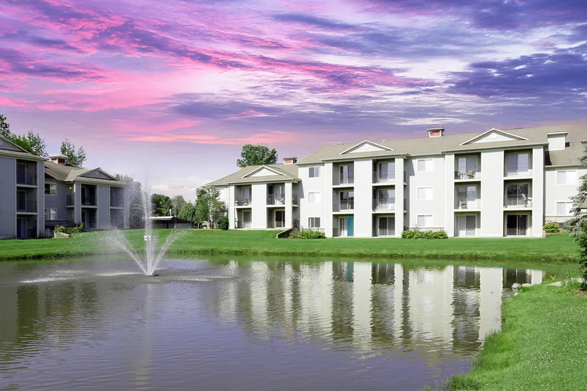 Charming apartment complex, Clearview Apartments, with serene pond view, vibrant sunset skies, and lush green surroundings.